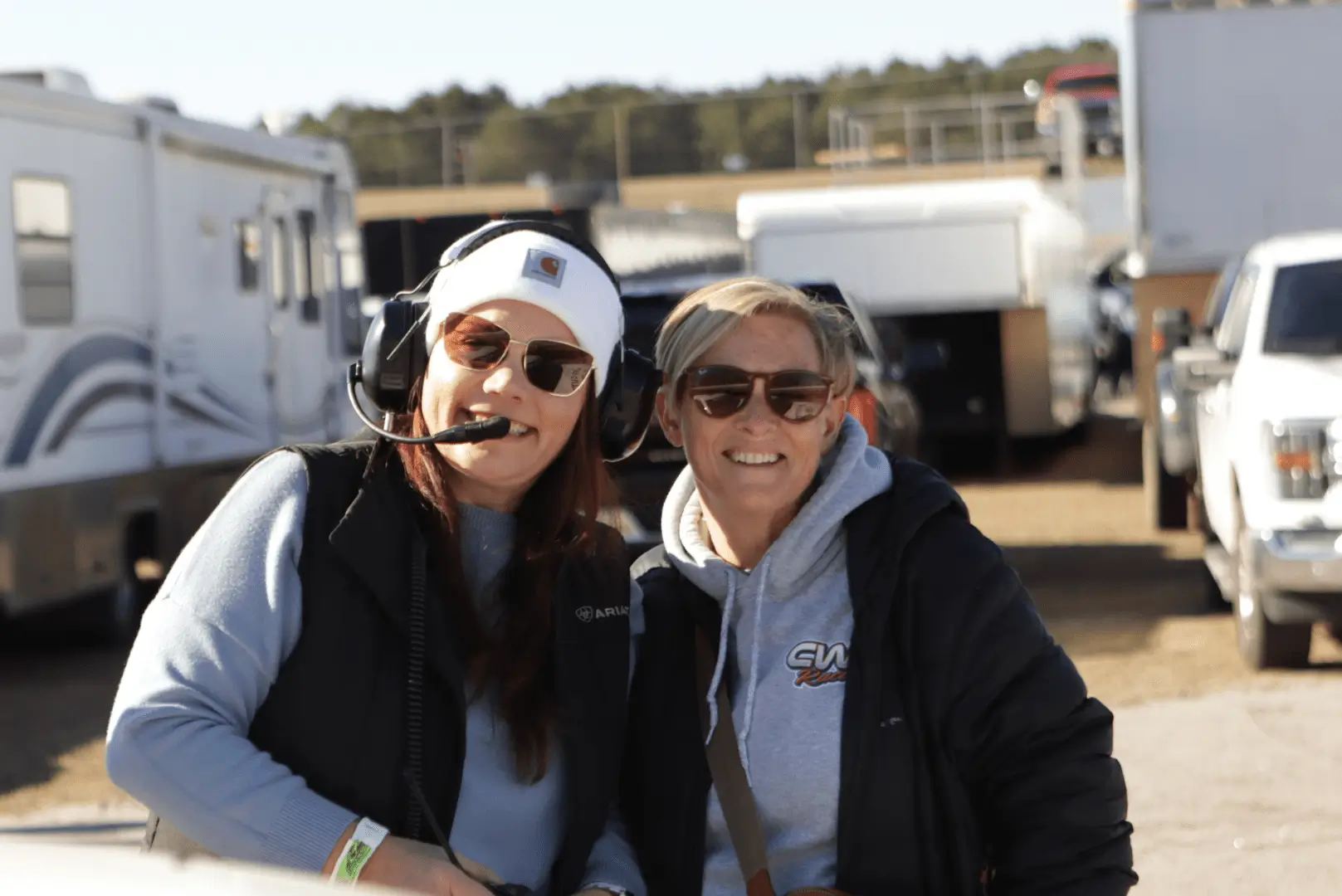 Two women are sitting in a field with their arms around each other.