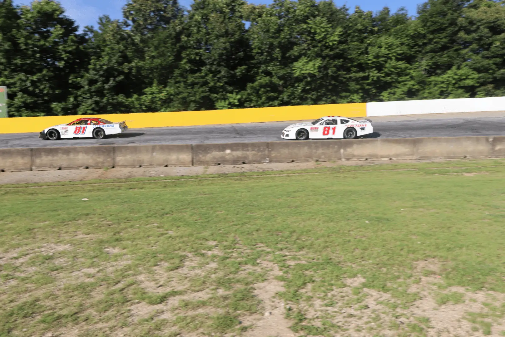Two cars are racing on a track near trees.